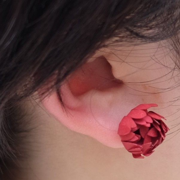 Nahaufnahme eines Ohrs einer Frau mit rotem Blumen-Ohrstecker.