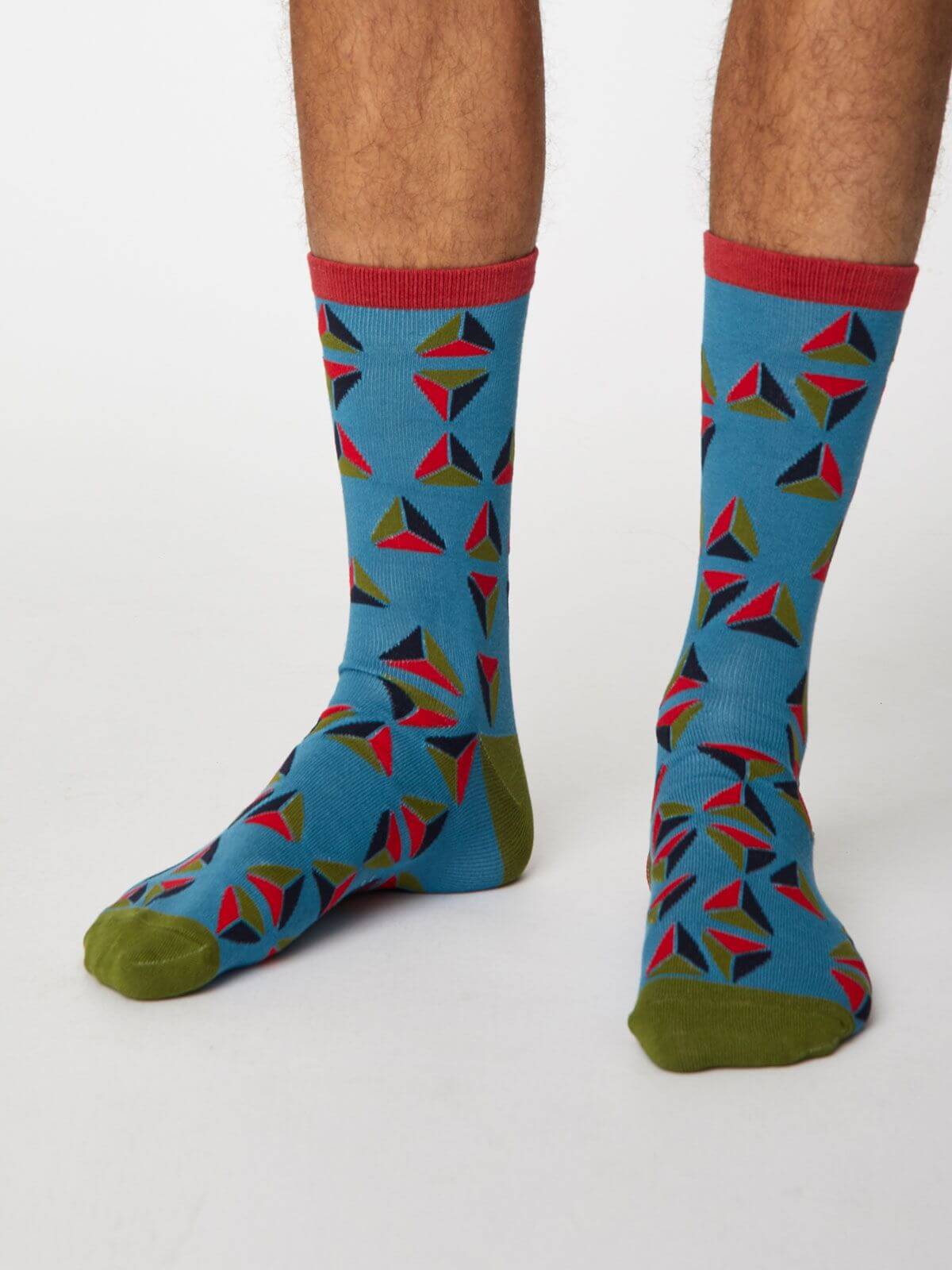 Model mit blauen Socken mit geometrischem Motiv in blau, rot und grün, an der Hacke und Spitze grün, am Bündchen rot.